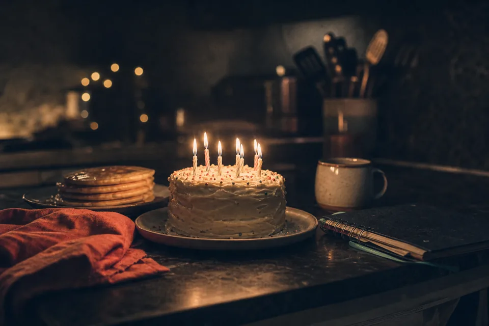 A candlelit birthday cake beside midnight pancakes and a college notebook